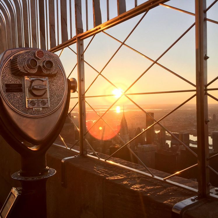 Binoculars next to a view of the sunrise at the Empire State Building